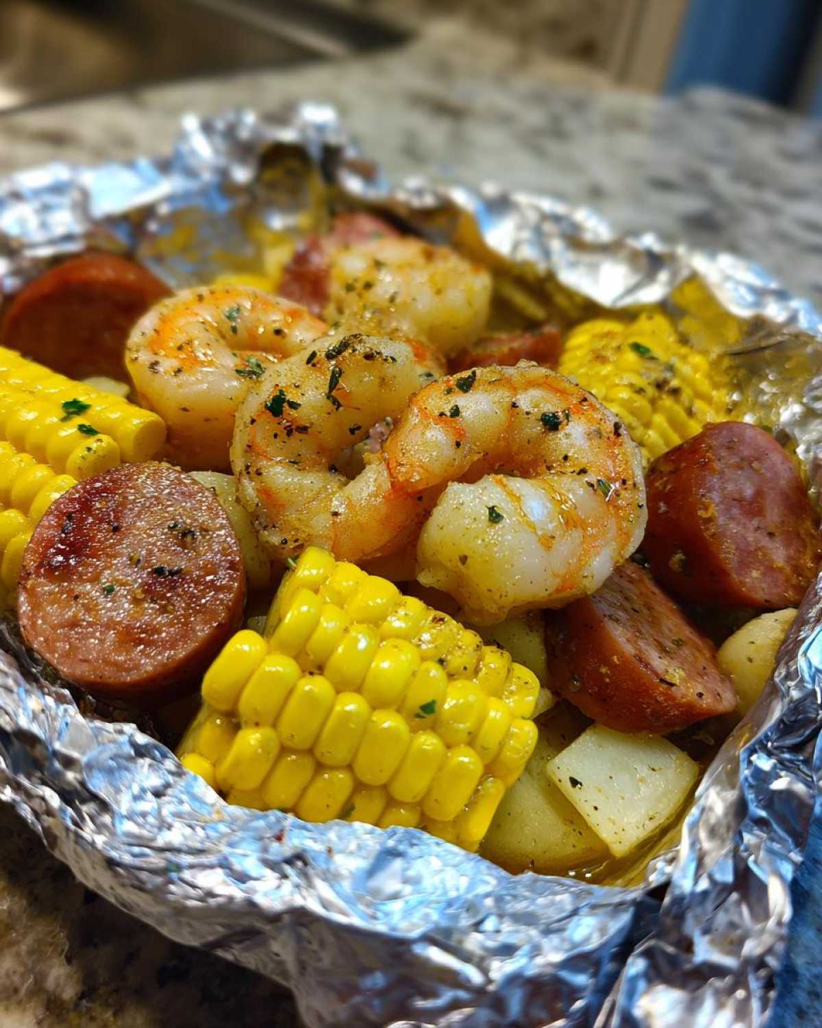 Close-up of cooked Shrimp Boil Foil Packets featuring seasoned shrimp, sliced sausage, corn on the cob, and potatoes.