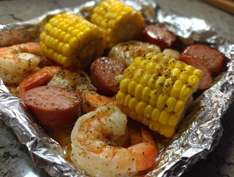 Close-up of cooked shrimp, sliced sausage, and corn on the cob seasoned in a foil packet for Shrimp Boil Foil Packets.