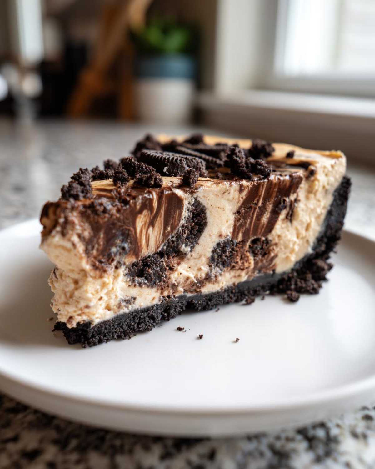 A decadent slice of Peanut Butter Fudge Ice Cream Pie featuring a dark cookie crust, swirled peanut butter and chocolate filling, topped with crushed cookies.