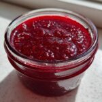 Close-up of bright red, glistening Small Batch Quick Raspberry Jam filling a small glass jar.