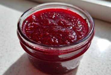 Close-up of bright red, glistening Small Batch Quick Raspberry Jam filling a small glass jar.