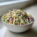 A large white bowl filled with fresh Southern Style Creamy Coleslaw featuring shredded green and purple cabbage and carrots.
