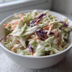 A white bowl filled with fresh Southern Style Creamy Coleslaw featuring shredded cabbage and carrots in a rich dressing.