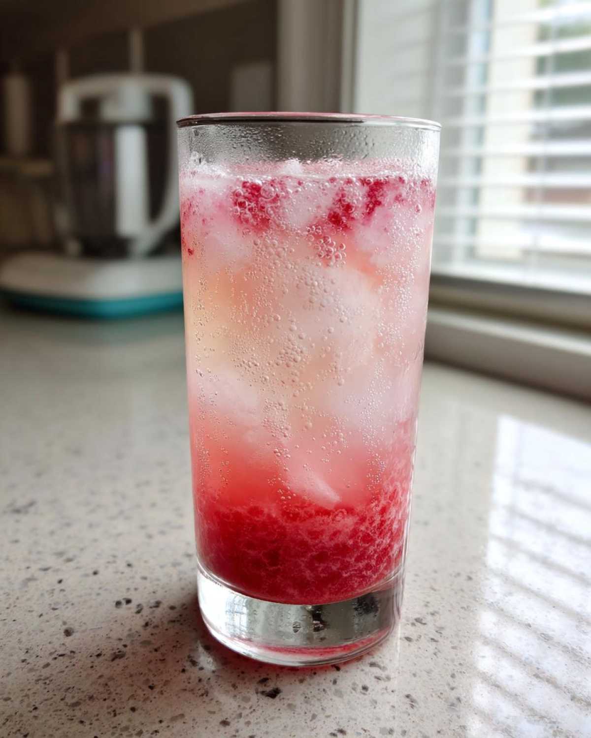 A tall glass filled with Sparkling Fresh Strawberry Lemonade, showing layers of crushed strawberries, ice, and carbonation.