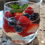 Close-up of a glass filled with Summer Berry White Wine Sangria, featuring strawberries, blueberries, raspberries, and mint.