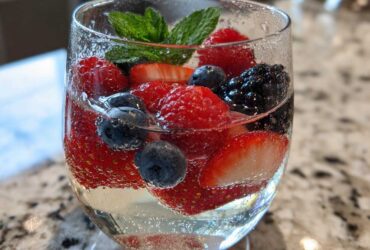 Close-up of a glass filled with Summer Berry White Wine Sangria, featuring strawberries, blueberries, raspberries, and mint.