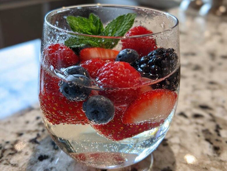 Close-up of a glass filled with Summer Berry White Wine Sangria, featuring strawberries, blueberries, raspberries, and mint.