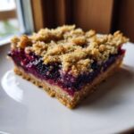 A close-up, delicious shot of a single serving of Sweet Blackberry Crumble Bars with a thick fruit layer and crumb topping.