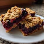 Three delicious Sweet Blackberry Crumble Bars stacked slightly on a white plate, showing the thick blackberry filling and oat topping.
