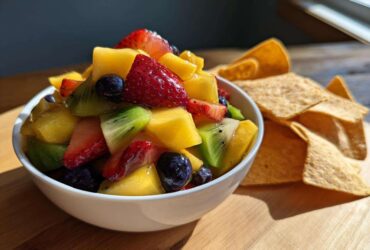 A white bowl filled with Sweet Fresh Fruit Salsa next to a pile of cinnamon tortilla chips on a wooden board.
