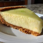 A perfect slice of Tangy Key Lime Pie showing the creamy filling and thick graham cracker crust, topped with lime zest.