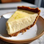Close-up of a perfect slice of Tangy Key Lime Pie showing the creamy filling and graham cracker crust, topped with lime zest.