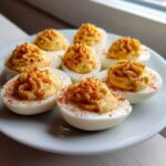 Seven halves of Traditional Deviled Eggs, piped high with creamy filling and sprinkled with paprika, served on a white plate.