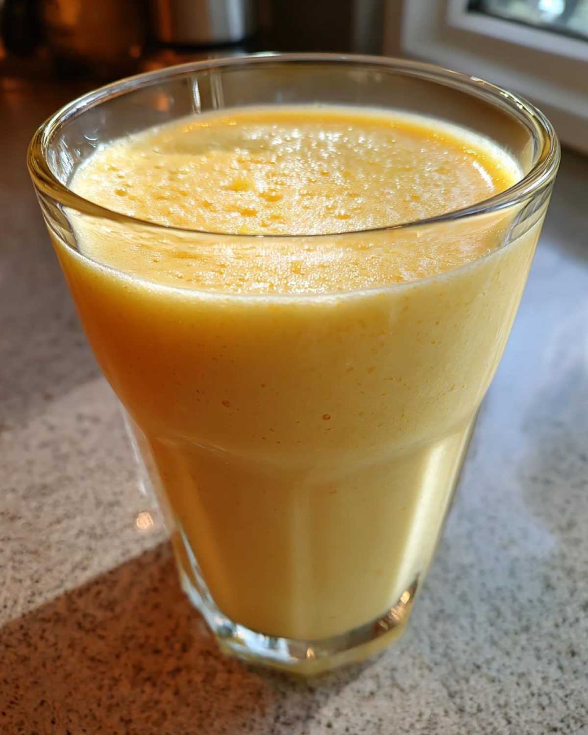 A close-up of a thick, vibrant yellow Tropical Pineapple Coconut Smoothie served in a clear glass.
