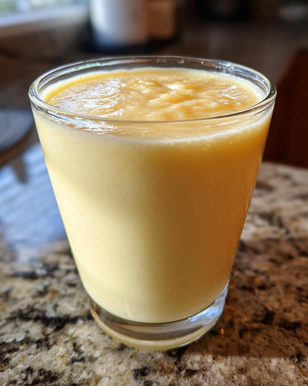 Close-up of a glass filled with a thick, creamy Tropical Pineapple Coconut Smoothie on a granite countertop.