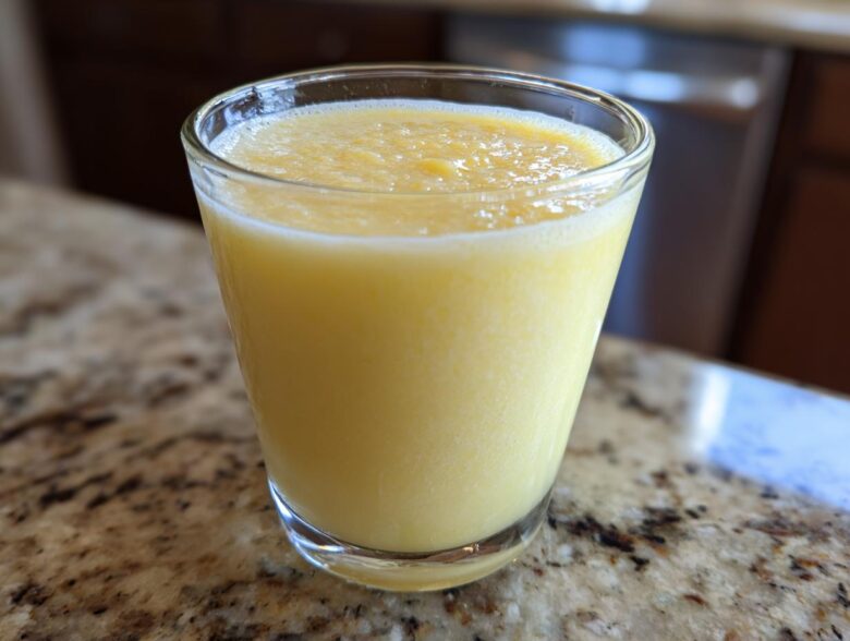 Close-up of a bright yellow Tropical Pineapple Coconut Smoothie served in a clear glass on a granite countertop.