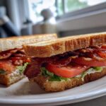 A close-up of The Ultimate BLT Sandwich on Toasted Bread, cut in half and stacked high with crispy bacon, tomato, and lettuce.