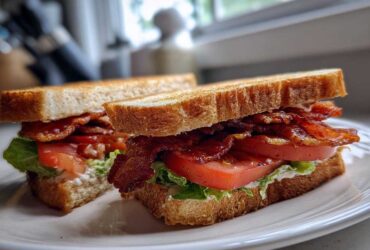 A close-up of The Ultimate BLT Sandwich on Toasted Bread, cut in half and stacked high with crispy bacon, tomato, and lettuce.