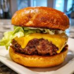 Close-up of an Ultimate Juicy Grilled Beef Burger featuring a thick, charred patty, melted cheddar cheese, lettuce, and a toasted brioche bun.