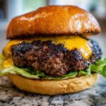 Close-up of an Ultimate Juicy Grilled Beef Burger featuring a thick, seared patty topped with melted cheddar cheese and crisp lettuce on a brioche bun.